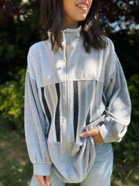 Person wearing a gray zip-up sweatshirt with a black and white pattern, standing outdoors.