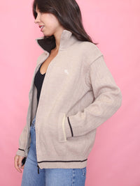 Model wearing a vintage neutral zip-up knit cardigan with ribbed texture, black trim, and a cosy unisex fit – ideal autumn wardrobe staple.