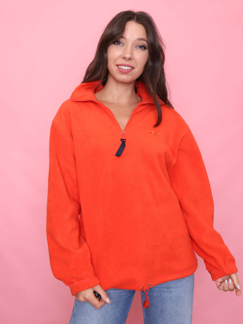 Model wearing a bright orange vintage Asics 1/4 zip fleece with embroidered logo and toggle hem. Cosy sporty outdoorswear.