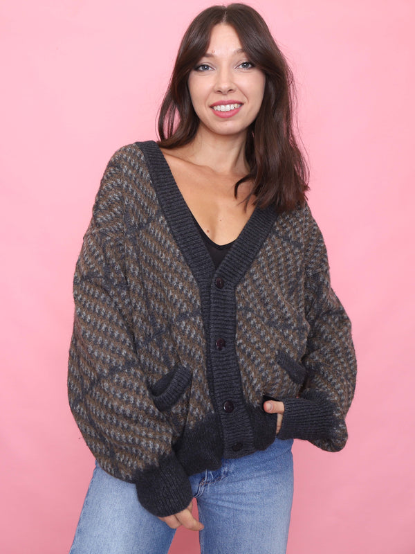 Model wearing a vintage brown and navy geometric knit cardigan with ribbed cuffs, deep pockets, and oversized unisex fit.