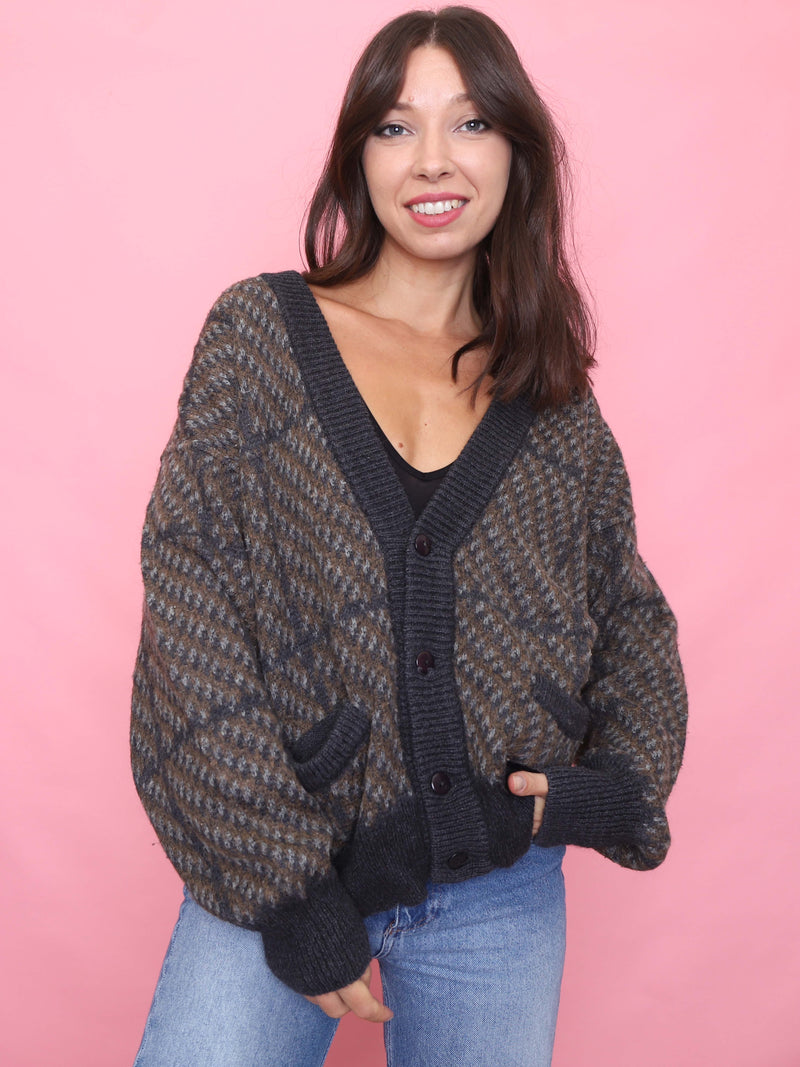 Model wearing a vintage brown and navy geometric knit cardigan with ribbed cuffs, deep pockets, and oversized unisex fit.