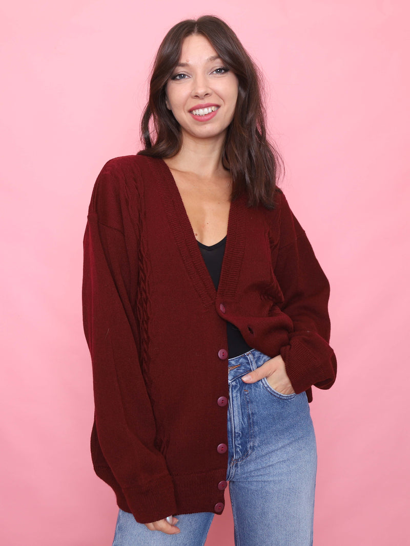 Model wearing a deep burgundy vintage cardigan with buttons and light wash jeans on a pink background.

