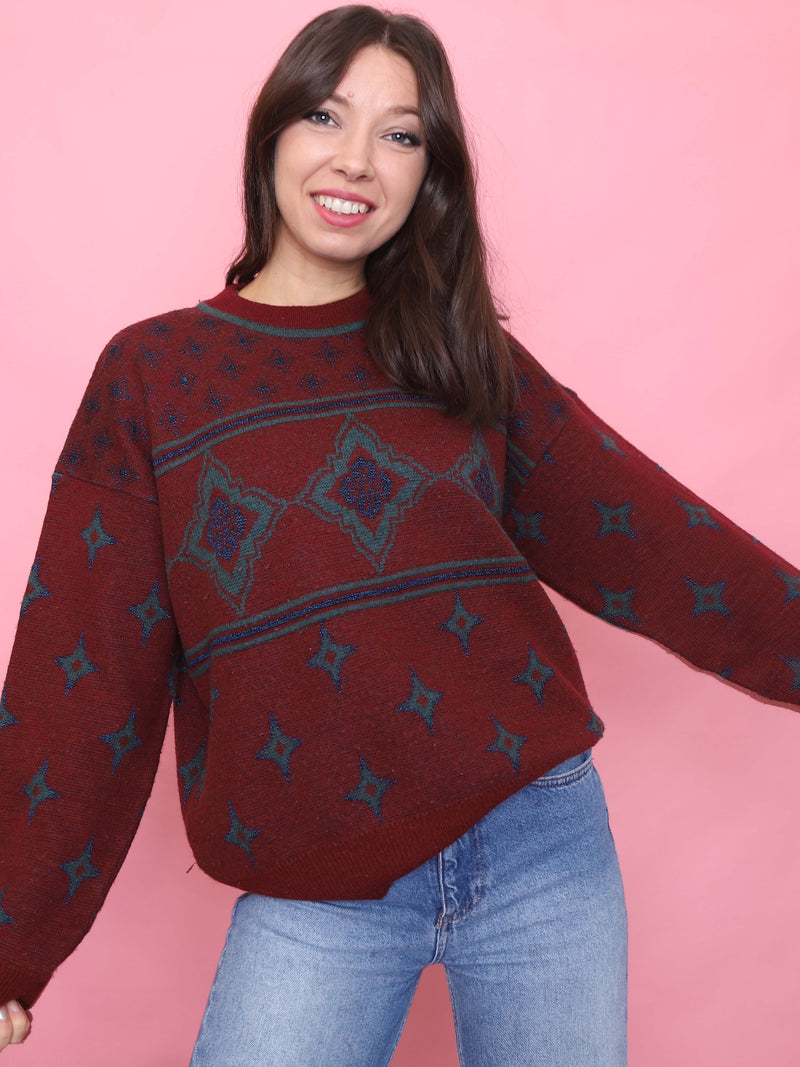 Model wearing a vintage burgundy jumper with teal star and geometric patterns, styled for autumn


