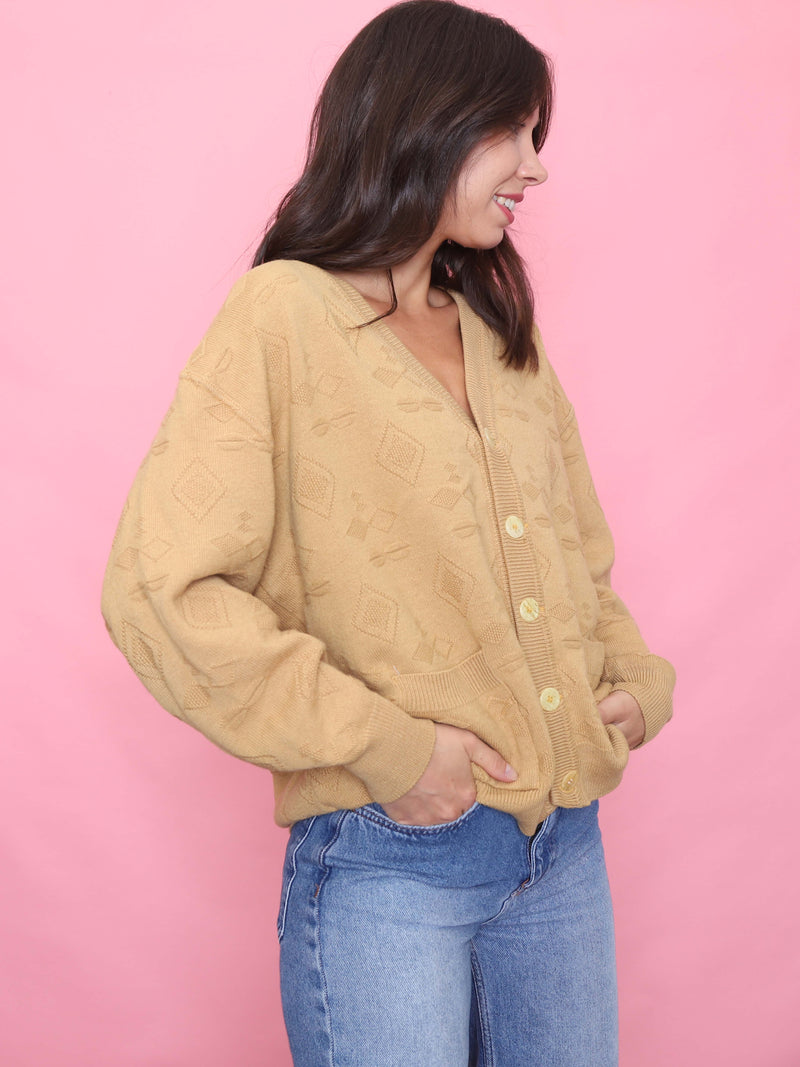 Model wearing a camel-toned vintage cardigan with textured diamond knit pattern and relaxed fit, styled with light-wash jeans.