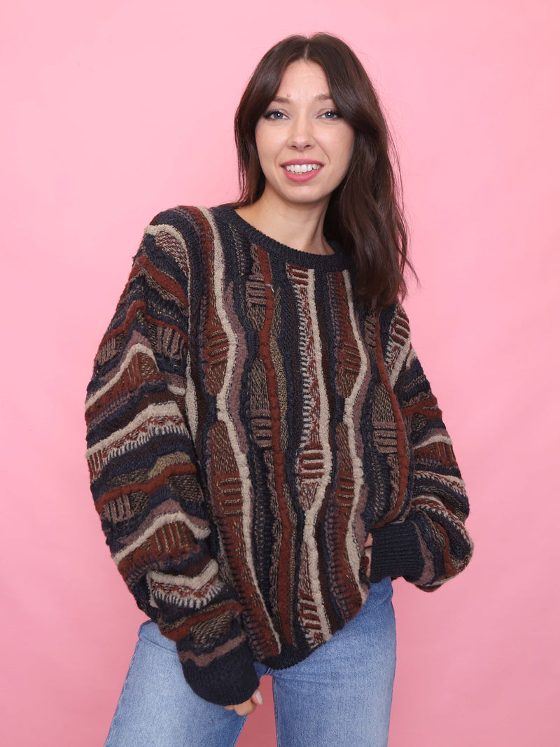 Woman wearing a vintage chunky knit jumper with bold textured pattern in earthy tones of brown, rust, beige and black

