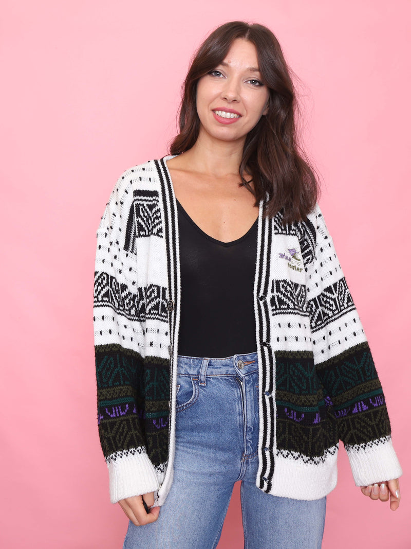 Model wearing a vintage black and white patterned knit cardigan with green and purple accents and an embroidered disco skater motif.