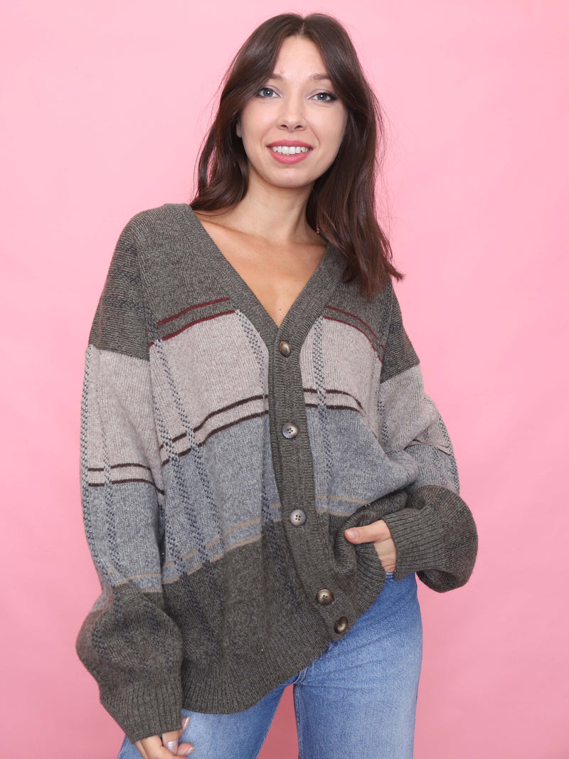 Model wears a slouchy vintage knit cardigan with earthy olive and grey stripes and wooden buttons, styled with light denim.