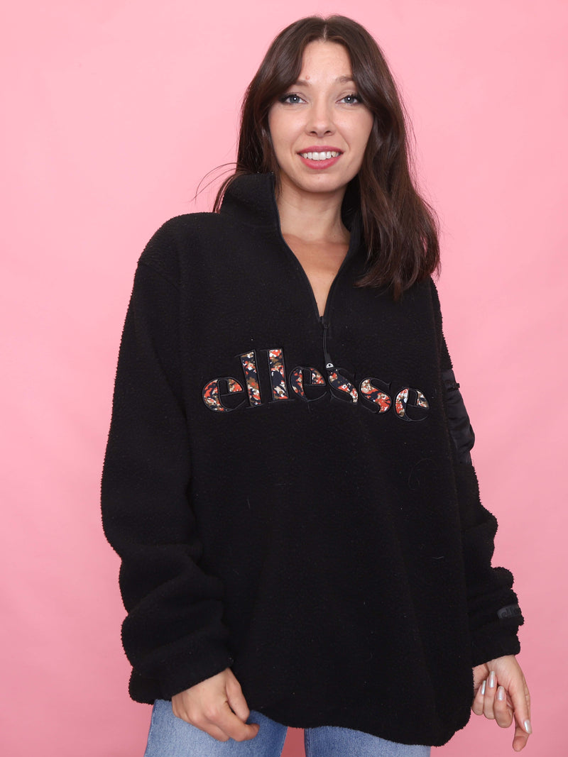 Model wearing a vintage black Ellesse teddy fleece with 1/4 zip and floral embroidered logo – cosy retro sports pullover.