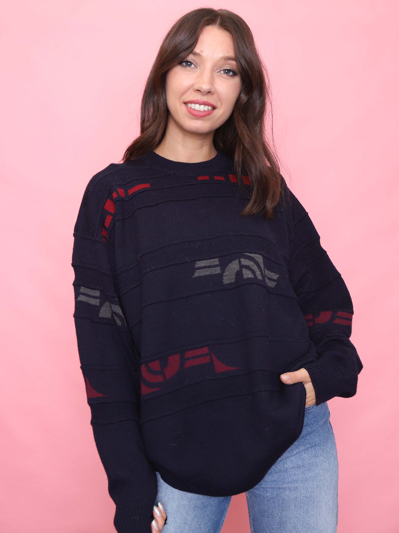 Woman wearing a dark blue sweater with red and gray patterns against a pink background
