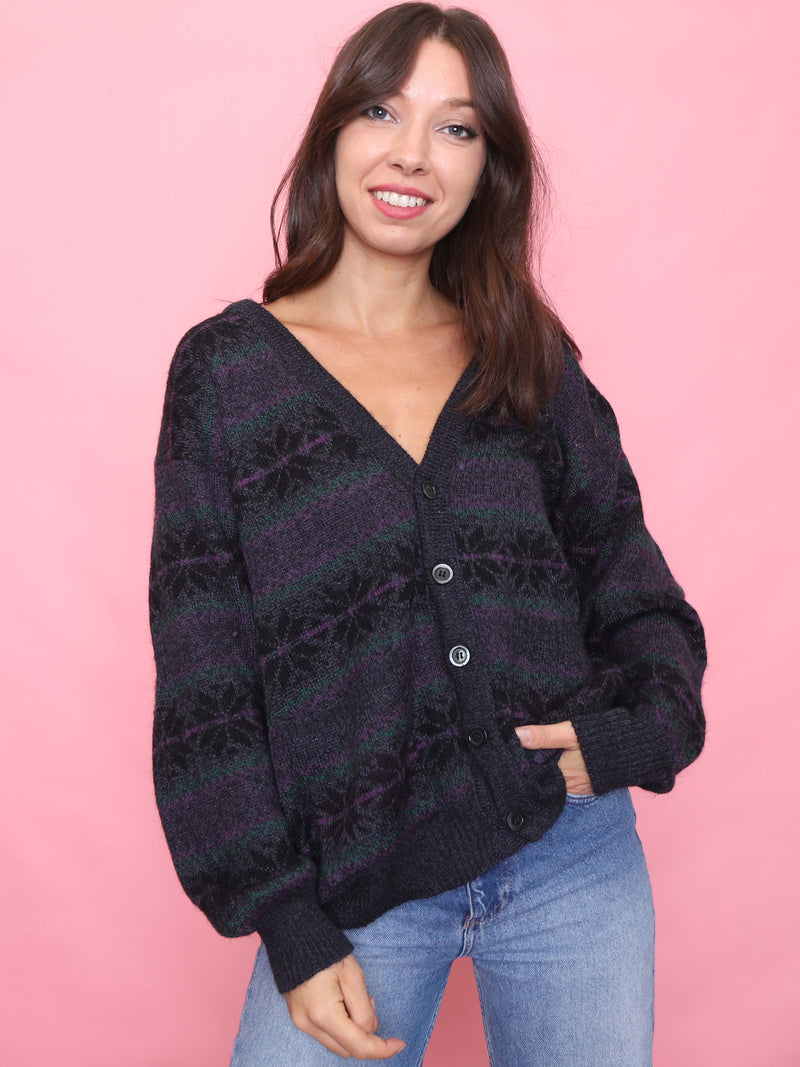 Model wearing a vintage black knit cardigan with purple and green snowflake pattern, relaxed unisex fit and button front.

