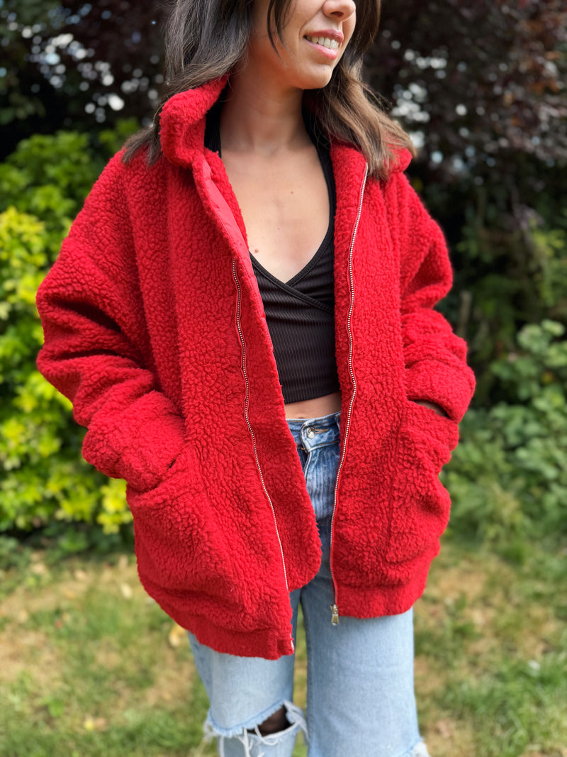 Model wearing an oversized vintage red teddy fleece zip-up jacket with deep pockets and cosy sherpa texture