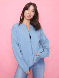 Model wearing a vintage soft blue zip-up cardigan with ribbed collar and cuffs, styled with light denim jeans on a pink background.